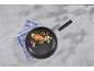 Frying pan with chicken and vegetables on a grey background, blue towel beside it
