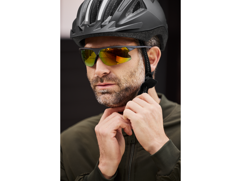Man in a cycling helmet and sports sunglasses adjusting his jacket.