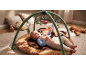 Baby playing on an activity mat with hanging toys and pillows in the background.