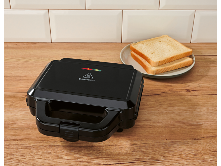 Black sandwich maker on a wooden countertop with toast on a plate.