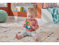 Baby sitting on a rug, playing with a sloth-shaped rattle.