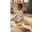 Baby in knitted romper sitting on a rug with toys in a nursery.