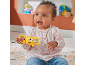 Smiling baby holding a yellow animal-shaped rattle, sitting on a rug.