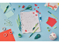 Green and red school supplies on a blue background, with a notebook featuring letters and hearts.