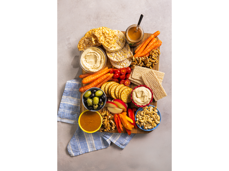 Snack board with hummus, carrots, crackers, nuts, and fruit