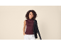 Women's sleeveless burgundy top with white trousers and black cardigan.