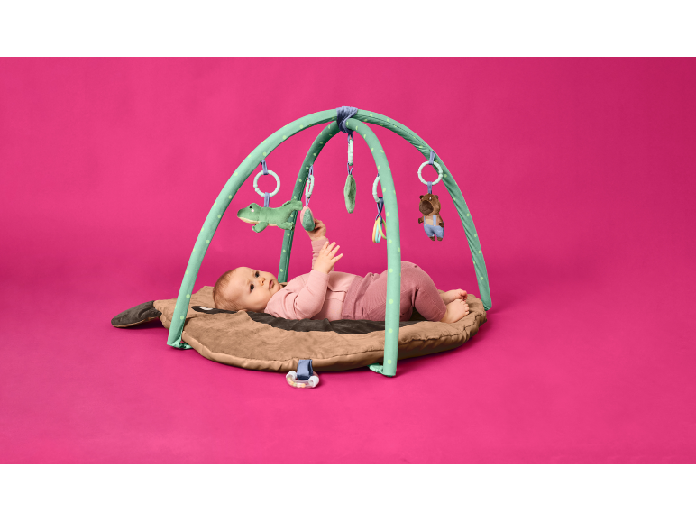 Baby lies on a play mat with arches, playing with hanging toys.
