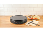 Electric crepe maker with banana and strawberry crepes on a wooden counter.