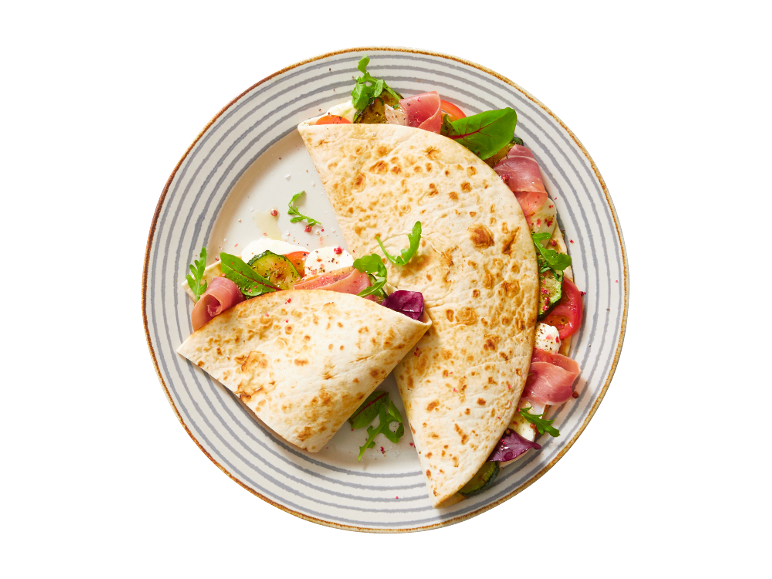 Piadina with ham, mozzarella, tomato, zucchini, and arugula on a striped plate.