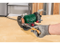 Green bench grinder with a wood chisel being sharpened by a gloved hand.