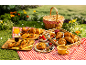 A picnic with a basket, croissants, pastries, berries, and drinks on a red checkered tablecloth.