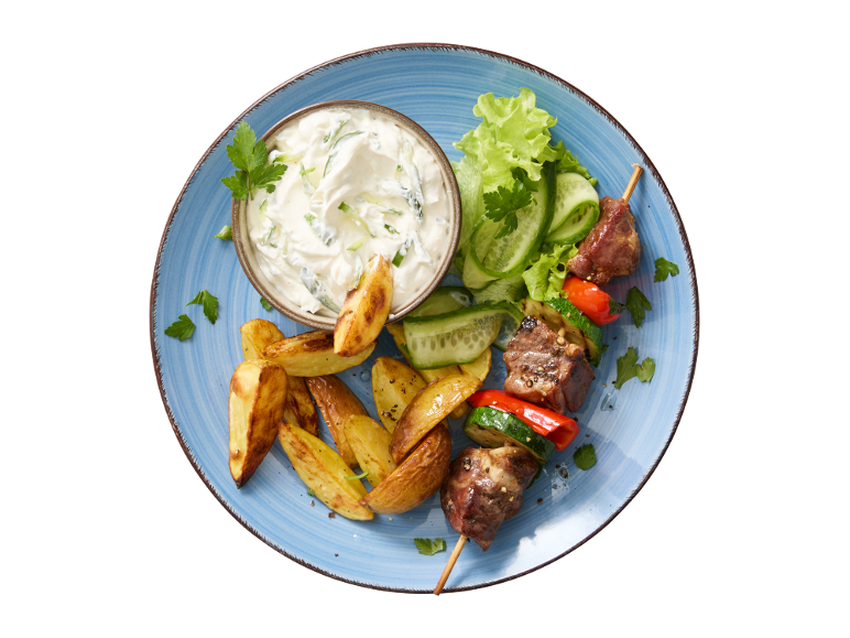 Meat and vegetable skewer, roasted potatoes, and tzatziki on a blue plate.
