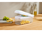 Cheese cutter with a clear container, filled with cheese cubes, next to grapes.