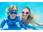 Two people wearing swim goggles and swimwear underwater, smiling at the camera.