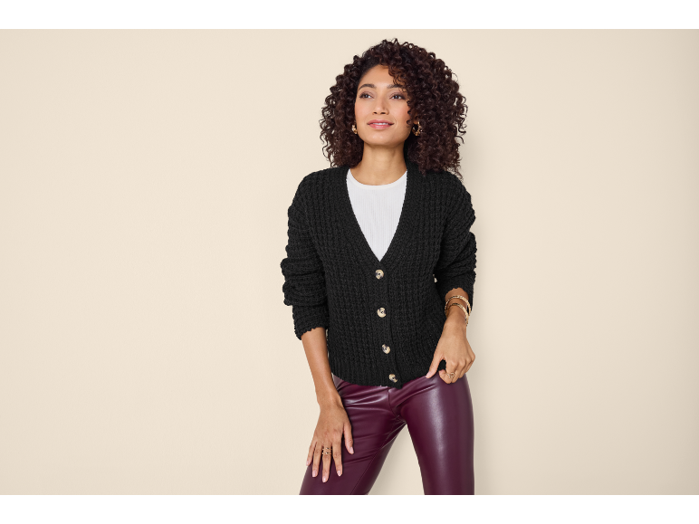 Woman in black knit cardigan, white t-shirt, and burgundy faux leather pants.