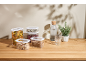 Transparent food containers with dry goods, water bottle, and plant on a wooden table.