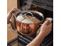 Hands placing a steaming pot with a reflective surface into an oven.