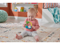 Baby sitting on a rug, playing with a sloth-shaped rattle.