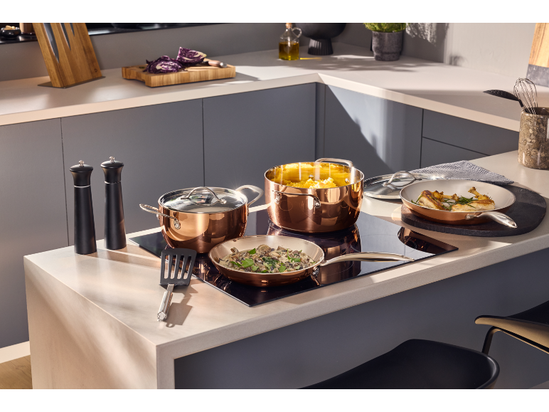 Copper pots and pans on an induction hob, with food and kitchen accessories.