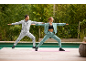Two people in tracksuits doing yoga outdoors by a pool.