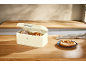 Bread and pretzels in a cream bread box on a wooden counter.
