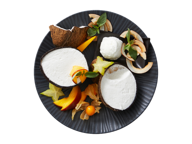 Coconut dessert with fresh fruit and toasted coconut flakes on a dark plate.