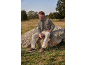 Man in olive green vest, plaid shirt, and beige trousers sitting on a rock.
