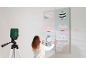 Woman uses a laser level to hang four children's pictures on a wall.