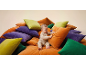 A baby sitting on a pile of colorful cushions in orange, purple, and green.
