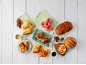 Assortment of baked goods and sandwiches, including donuts, croissants, and paninis, on a white wooden table.