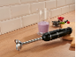 Black immersion blender with a smoothie in a measuring cup and berries on a wooden counter.