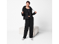 Woman in a black tracksuit with a hoodie and pants, posing next to an ottoman.