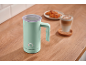 Mint green milk frother on a wooden counter with a latte and pastries.