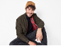 Man in a brown beanie, olive bomber jacket, black turtleneck, and dark jeans.