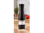 Black salt grinder with coarse salt on a wooden kitchen counter.