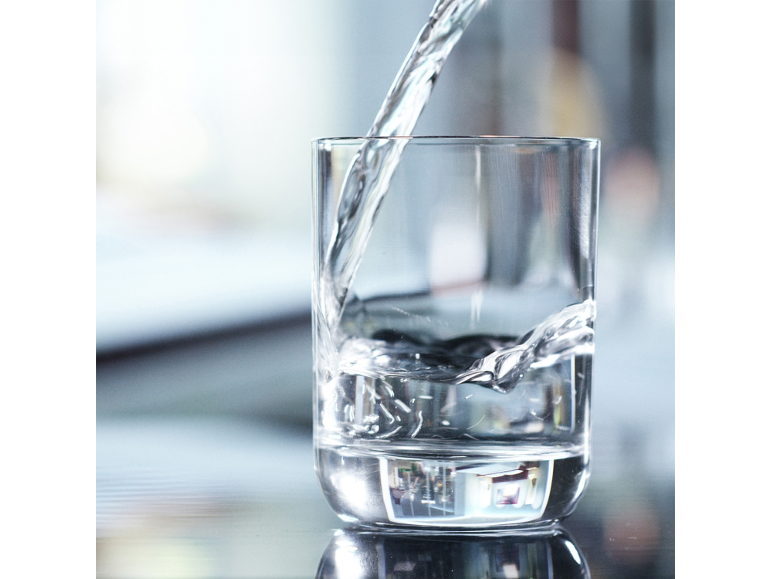 Transparent glass being filled with fresh, clear water.
