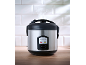 Steaming rice cooker with a metallic body and black lid on a wooden table.