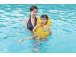 Smiling mother and child in a pool, child wearing a yellow swim vest.