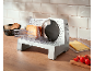 Electric slicer with a block of cheese, cheese slices, and cherry tomatoes.