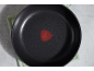 Black non-stick frying pan with heat indicator, on a green kitchen cloth.
