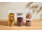 Transparent food containers with pasta, beans, rice, muesli, and lentils on a wooden table.