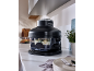 A black food steamer with a vegetable dish inside, placed on a kitchen counter.