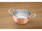 Copper-colored pot with stainless steel interior and measurement markings on a wooden table.