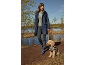 Woman in navy raincoat and boots, walking a dog in a leopard print coat by the water.