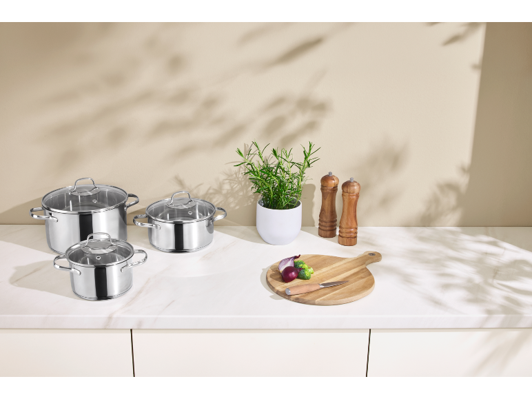 Stainless steel pot set with glass lids on a kitchen countertop.