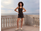 Woman in black tank top and black shorts on a balcony overlooking the sea.