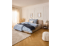 Bedroom with a bed featuring blue floral bedding, a beige rug, and a pouf.