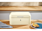 Cream-colored bread bin on a wooden counter with toast and a kitchen towel.
