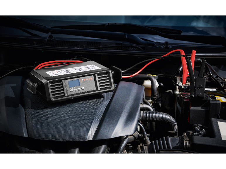 Car battery charger with jump leads connected to the engine