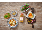 An all-purpose seasoning bottle on a wooden table with food dishes and garnishes.
